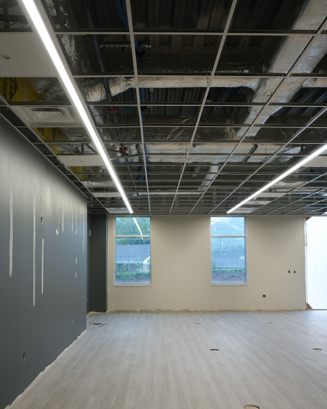 Partially completed ceiling grid, linear light fixtures, ductwork, and new flooring inside an administrative space at TCAT Jacksboro.